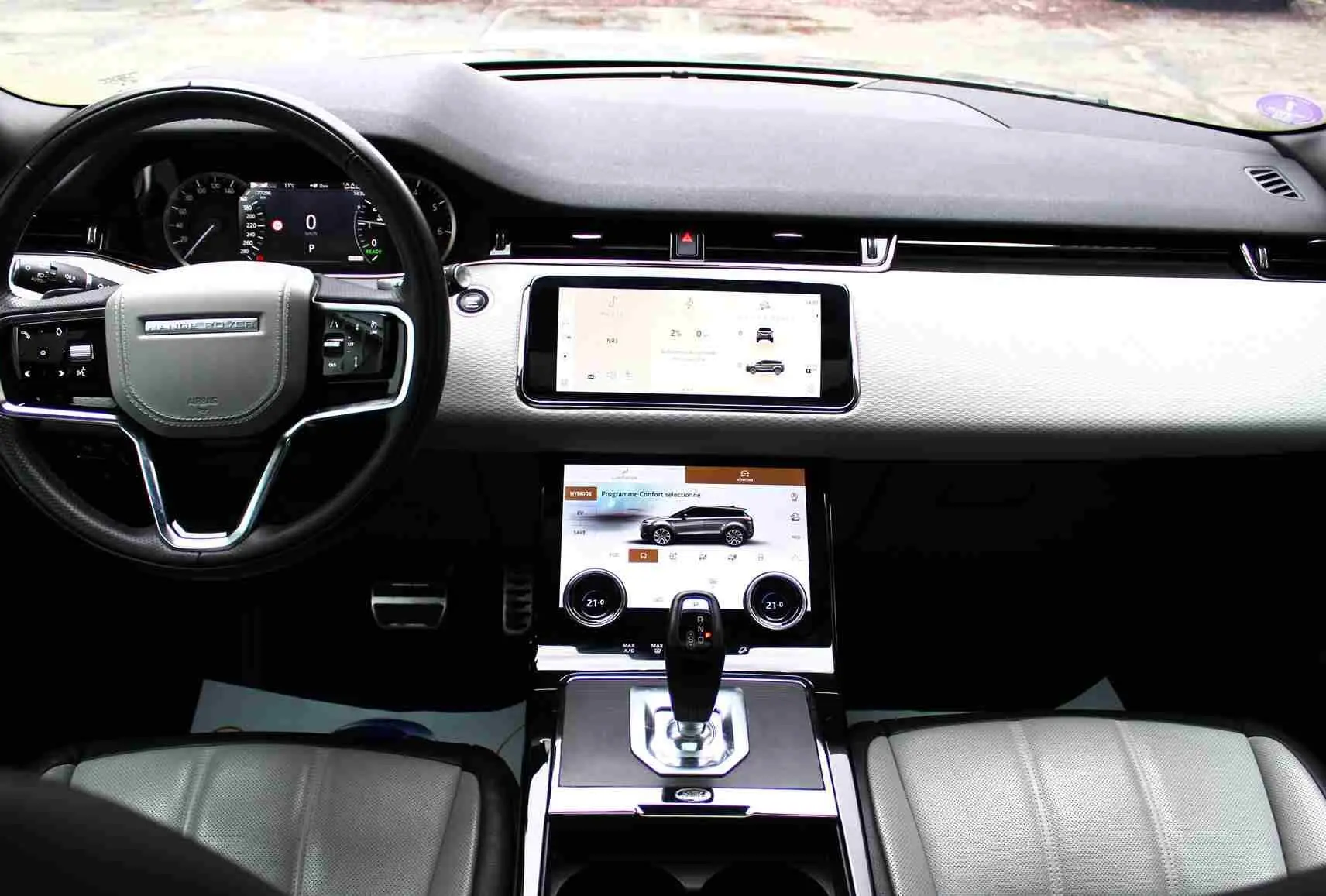 Intérieur du Range Rover Evoque 2023, vue de face sur le tableau de bord clair avec écran tactile et volant noir.