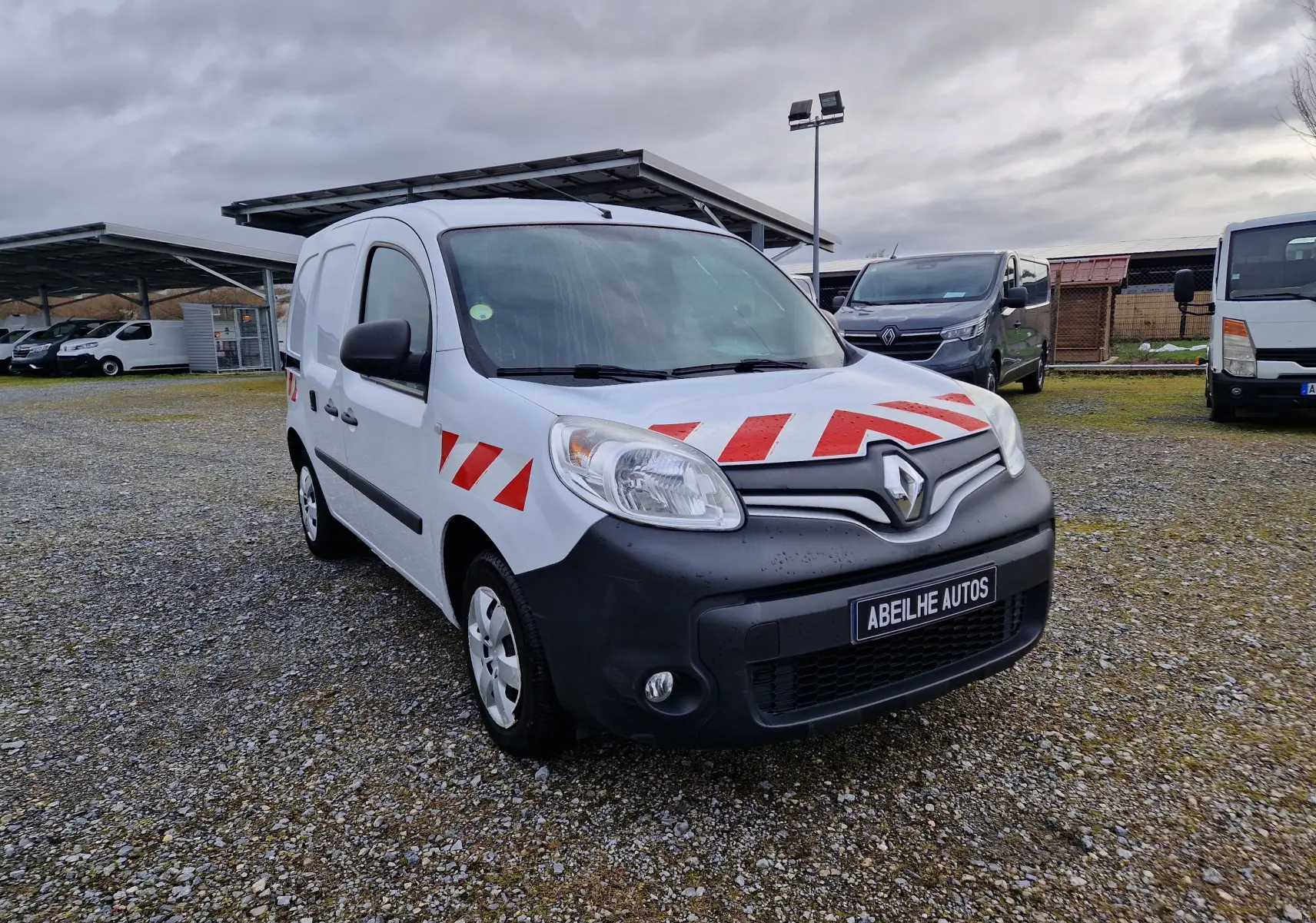Renault Kangoo blanc vue 3/4 avant droit avec bandes rouges réfléchissantes sur capot et portières.