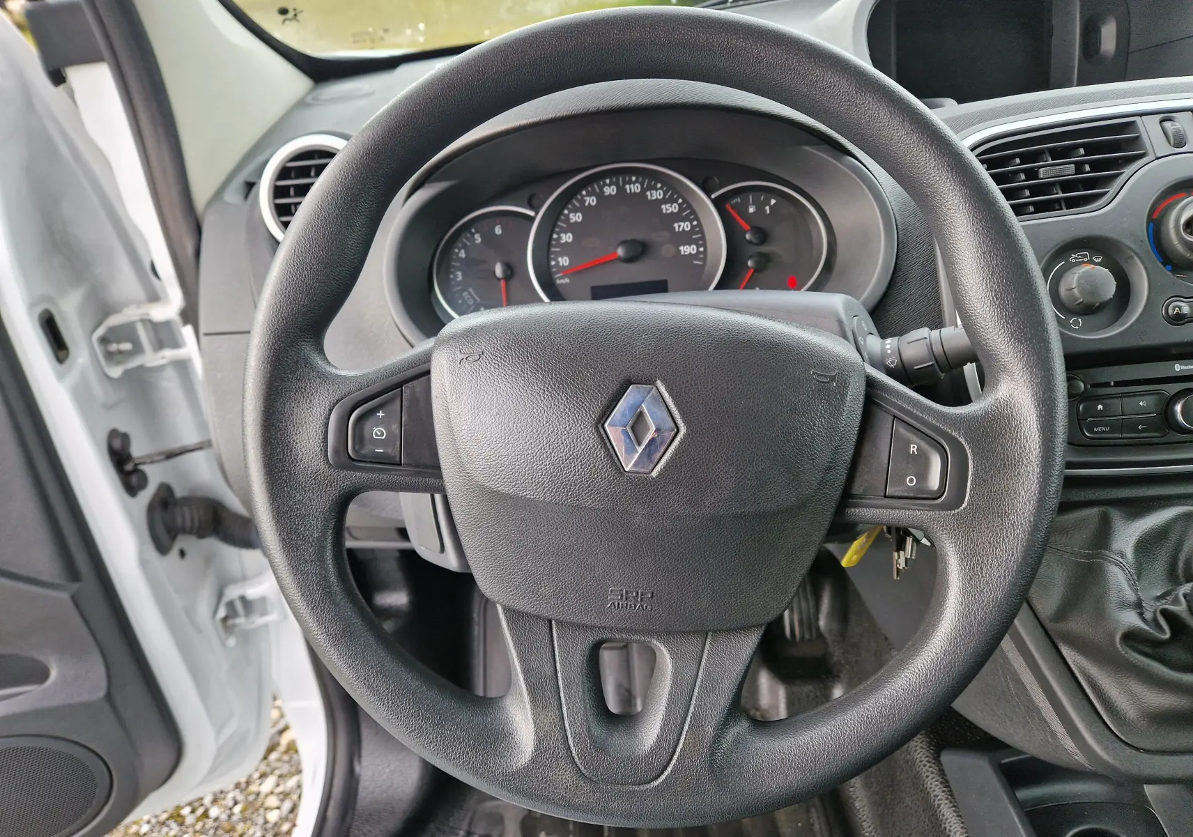 Vue intérieure centrée sur le volant noir avec logo Renault, tableau de bord et partie de la console d'une Renault Kangoo blanche 2019.