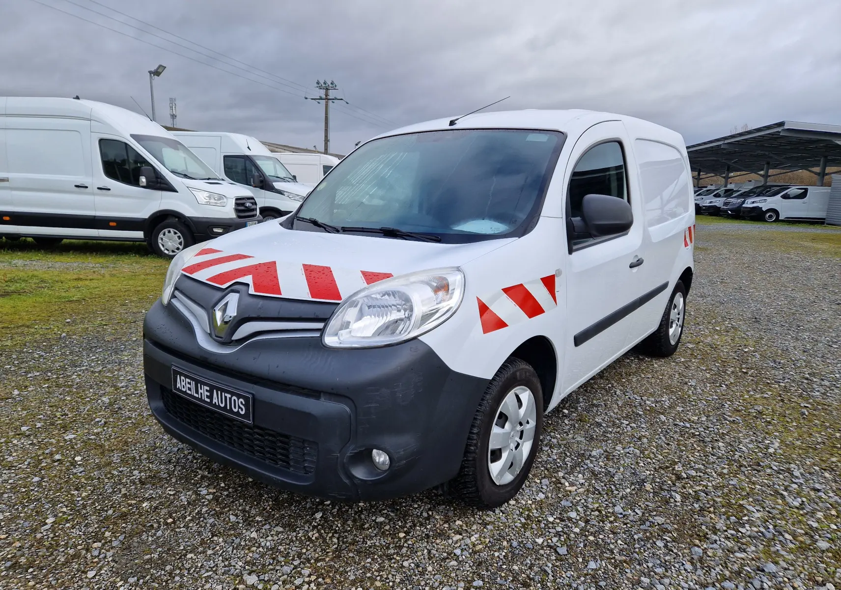 Renault Kangoo blanc vue 3/4 avant droit avec bandes rouges réfléchissantes sur capot et ailes.