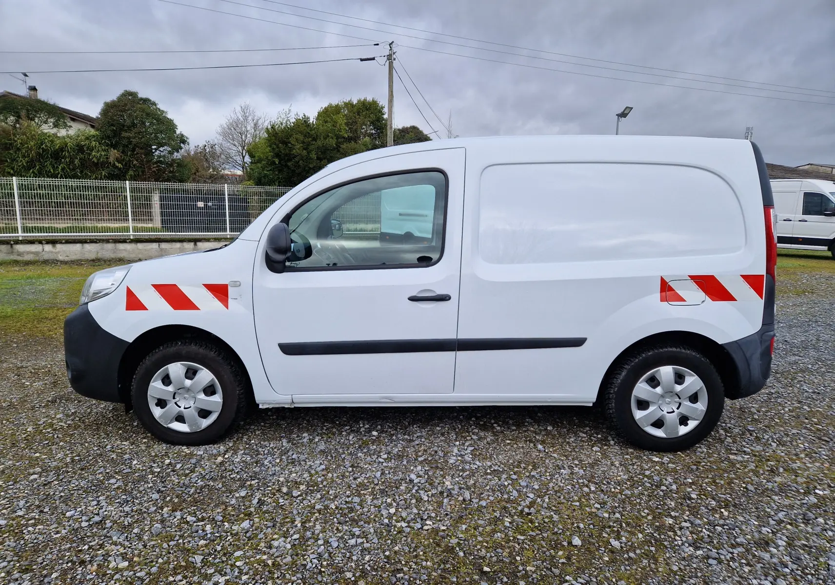 Vue latérale droite d’un Renault Kangoo blanc 2019 avec bandes réfléchissantes rouges sur ailes avant et arrière.