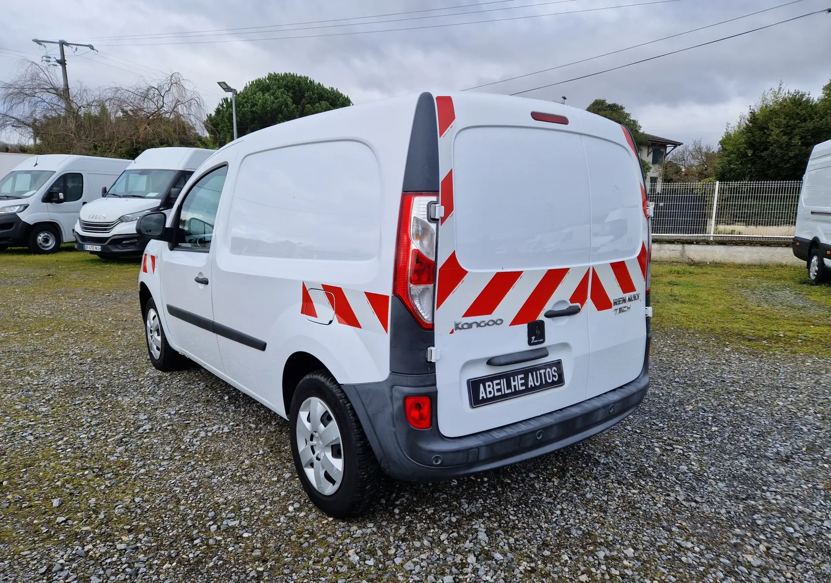 Renault Kangoo blanc vue 3/4 arrière droit avec bandes rouges réfléchissantes et plaque Abeilhe Autos.