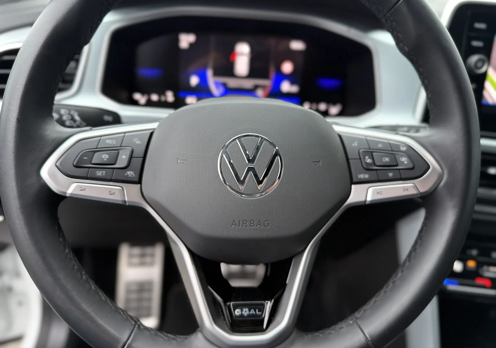 Gros plan sur le volant multifonction noir du Volkswagen T-Roc 2.0 TDI 150CH LIFE PLUS 2025 avec tableau de bord numérique flou en arrière-plan.