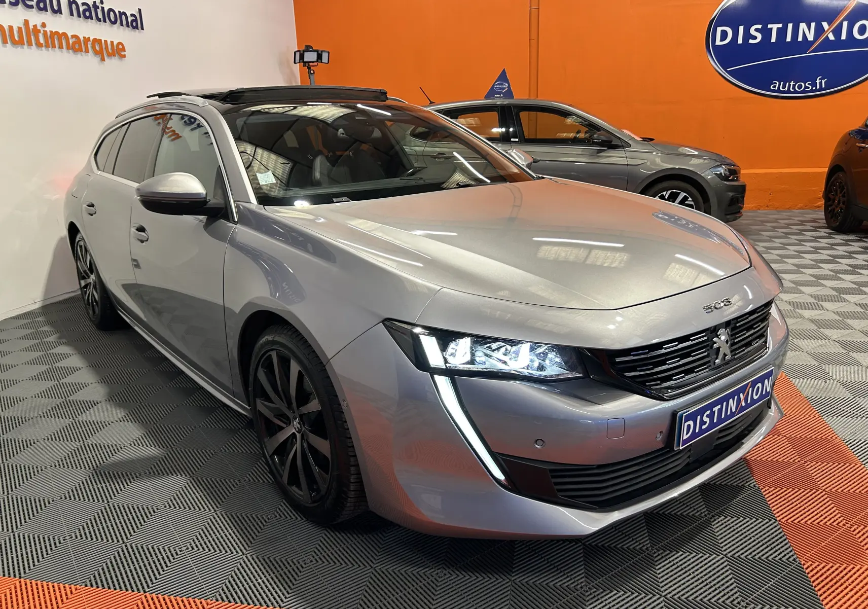 Peugeot 508 SW Gris Platinium vue 3/4 avant droit avec toit ouvrant et feux LED allumés en showroom.