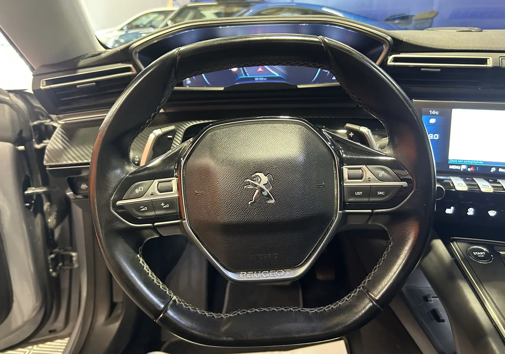 Vue rapprochée du volant cuir noir de la Peugeot 508 SW gris Platinium, avec tableau de bord digital et commandes intégrées.