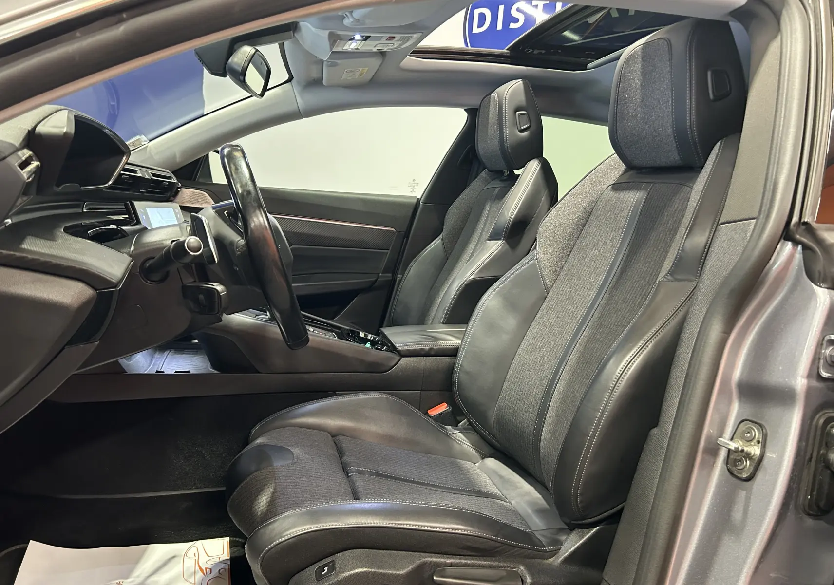 Vue intérieure côté conducteur de la Peugeot 508 SW gris Platinium, avec sièges cuir et toit ouvrant visible.