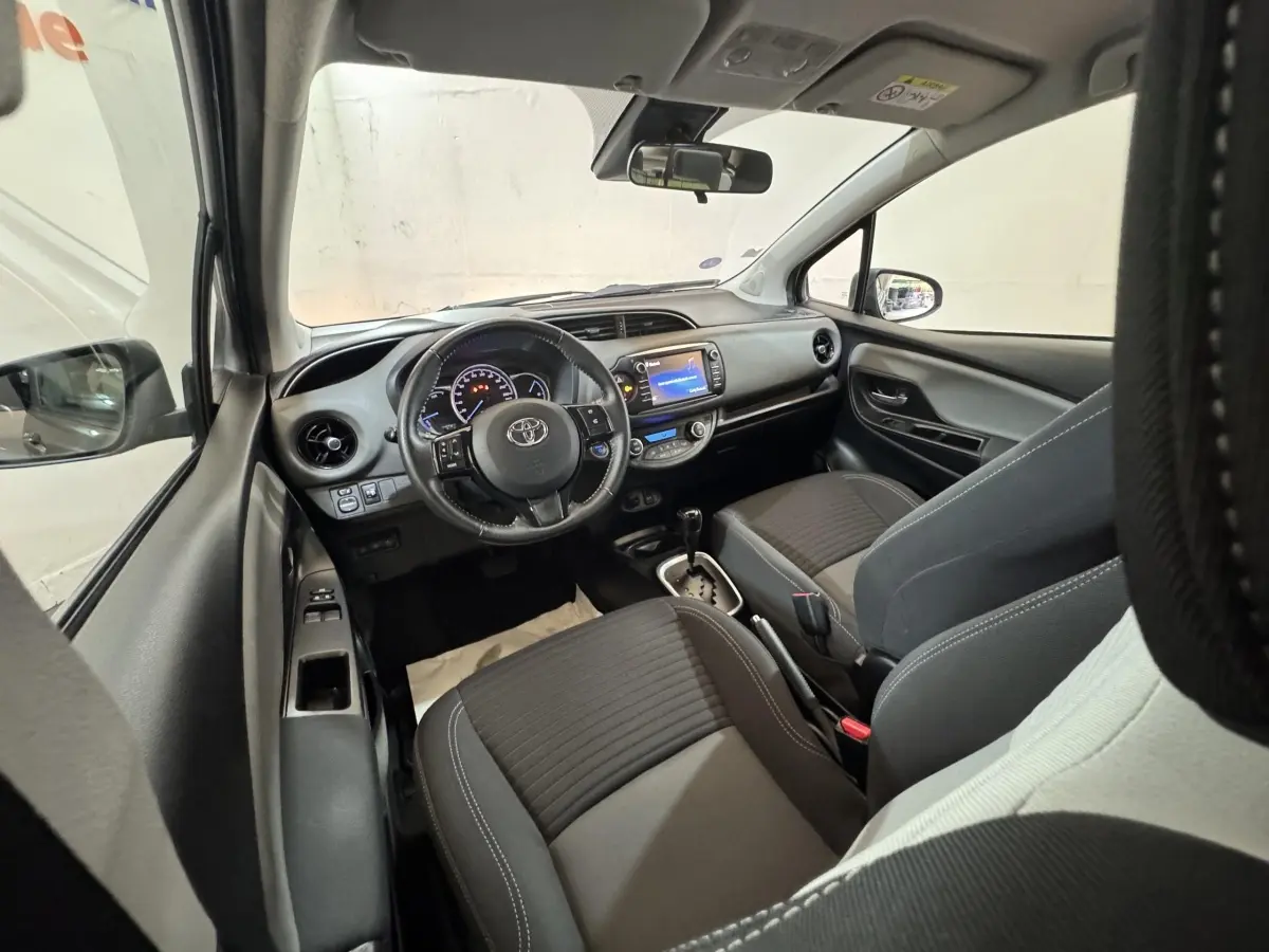 Vue intérieure avant de la Toyota Yaris 1.5 Hybrid 2019, montrant tableau de bord et sièges noirs avec volant multifonctions.