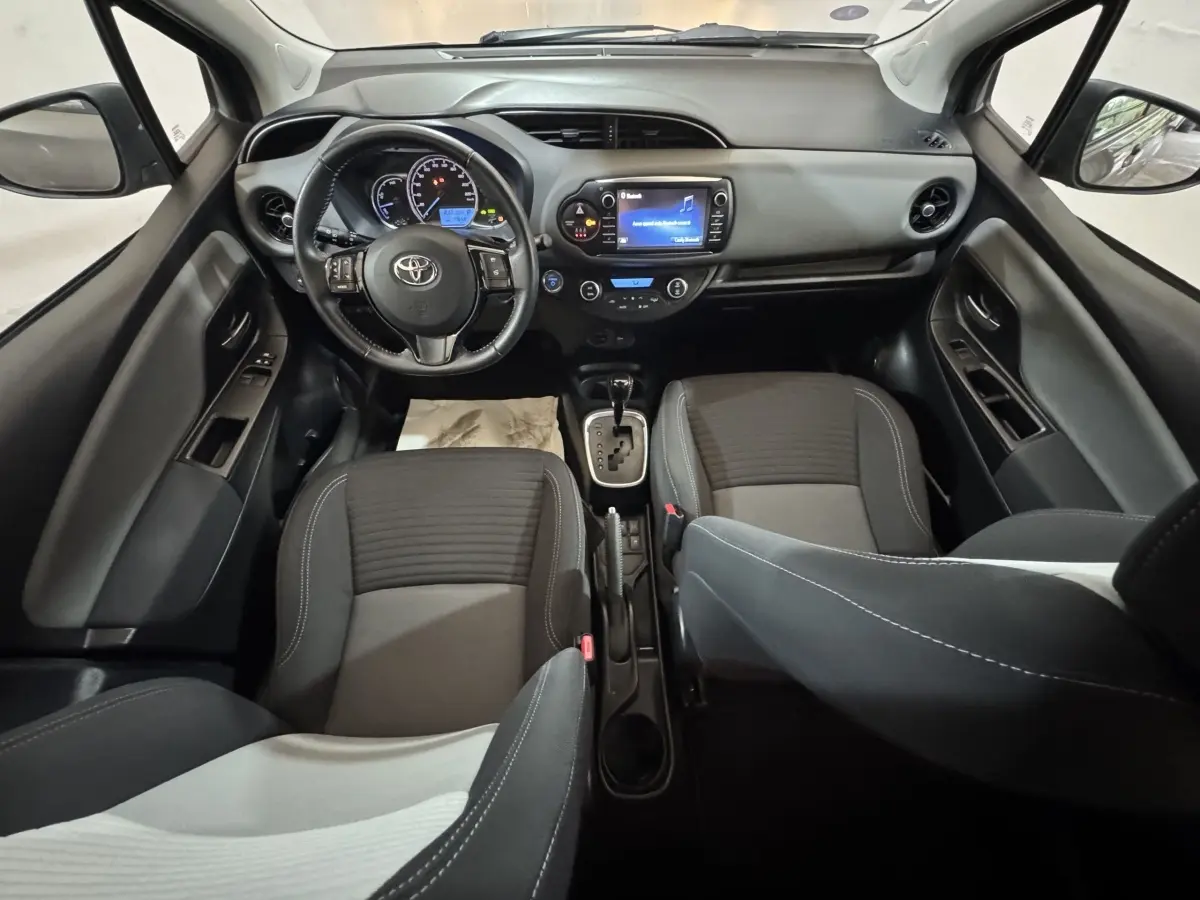 Vue intérieure avant de la Toyota Yaris 1.5 VVT-I Hybrid 2019, tableau de bord et sièges en tissu gris.
