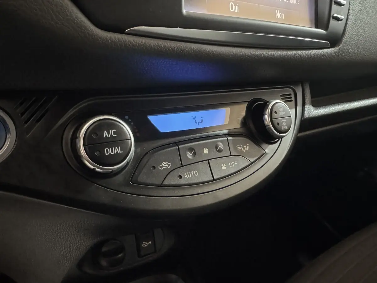 Gros plan sur la commande de climatisation digitale avec affichage bleu dans l'habitacle noir d'une Toyota Yaris gris foncé.
