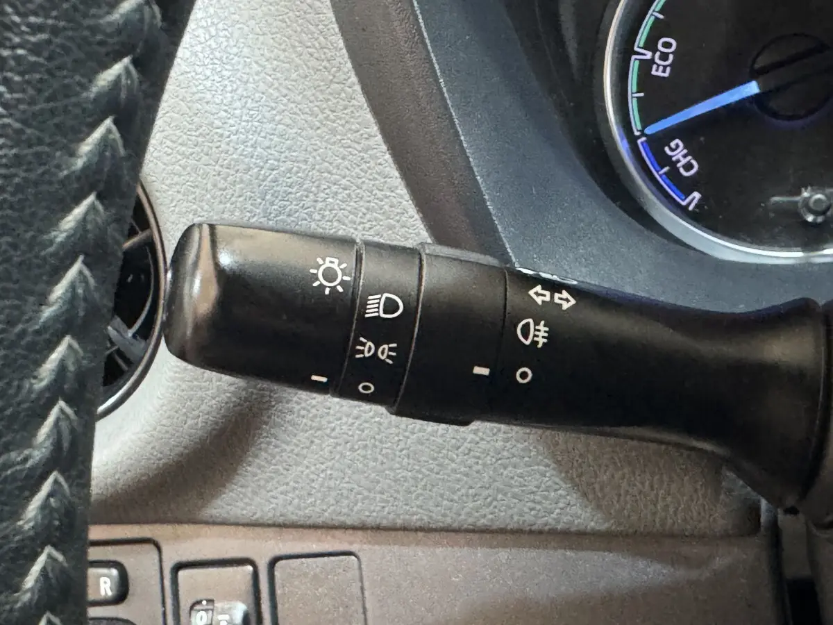 Gros plan sur la manette de commande des phares à gauche du volant dans l’habitacle gris d’une Toyota Yaris hybride 2019.