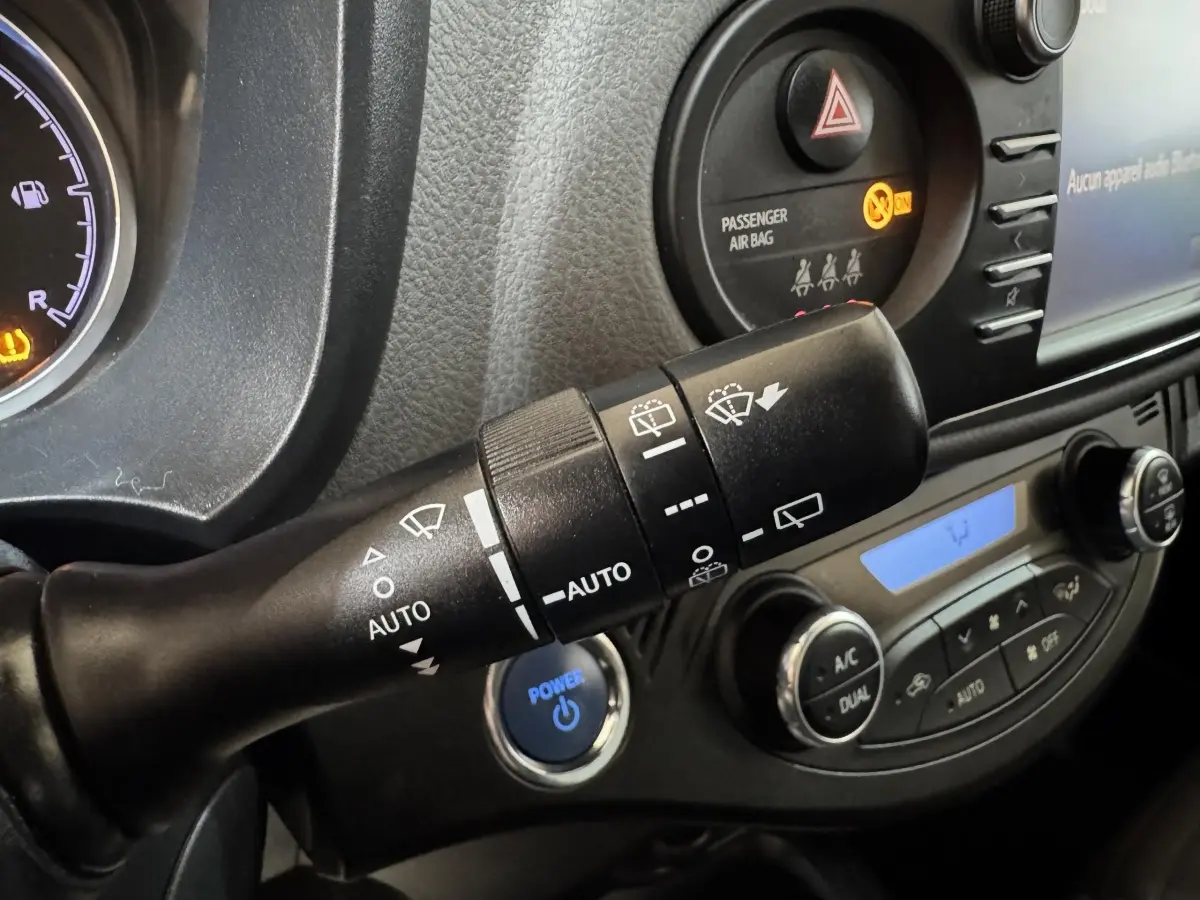 Gros plan sur la commande d’essuie-glace et le bouton démarrage bleu dans l’habitacle d’une Toyota Yaris gris foncé.
