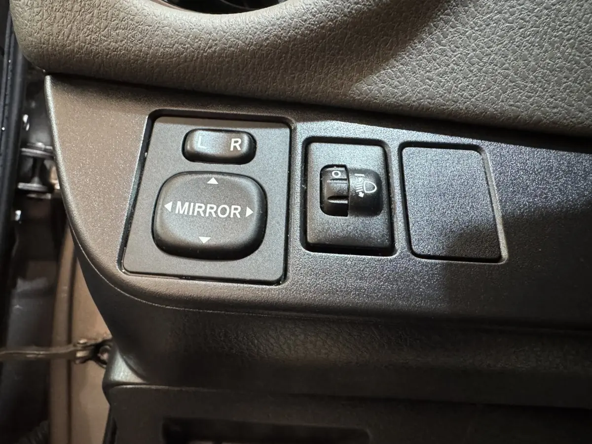Gros plan sur les commandes de réglage des rétroviseurs et des phares sur la porte côté conducteur d'une Toyota Yaris gris foncé.
