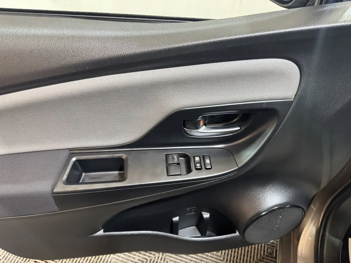 Vue intérieure côté conducteur de la porte d'une Toyota Yaris gris foncé, avec commandes de vitres et poignée noire.