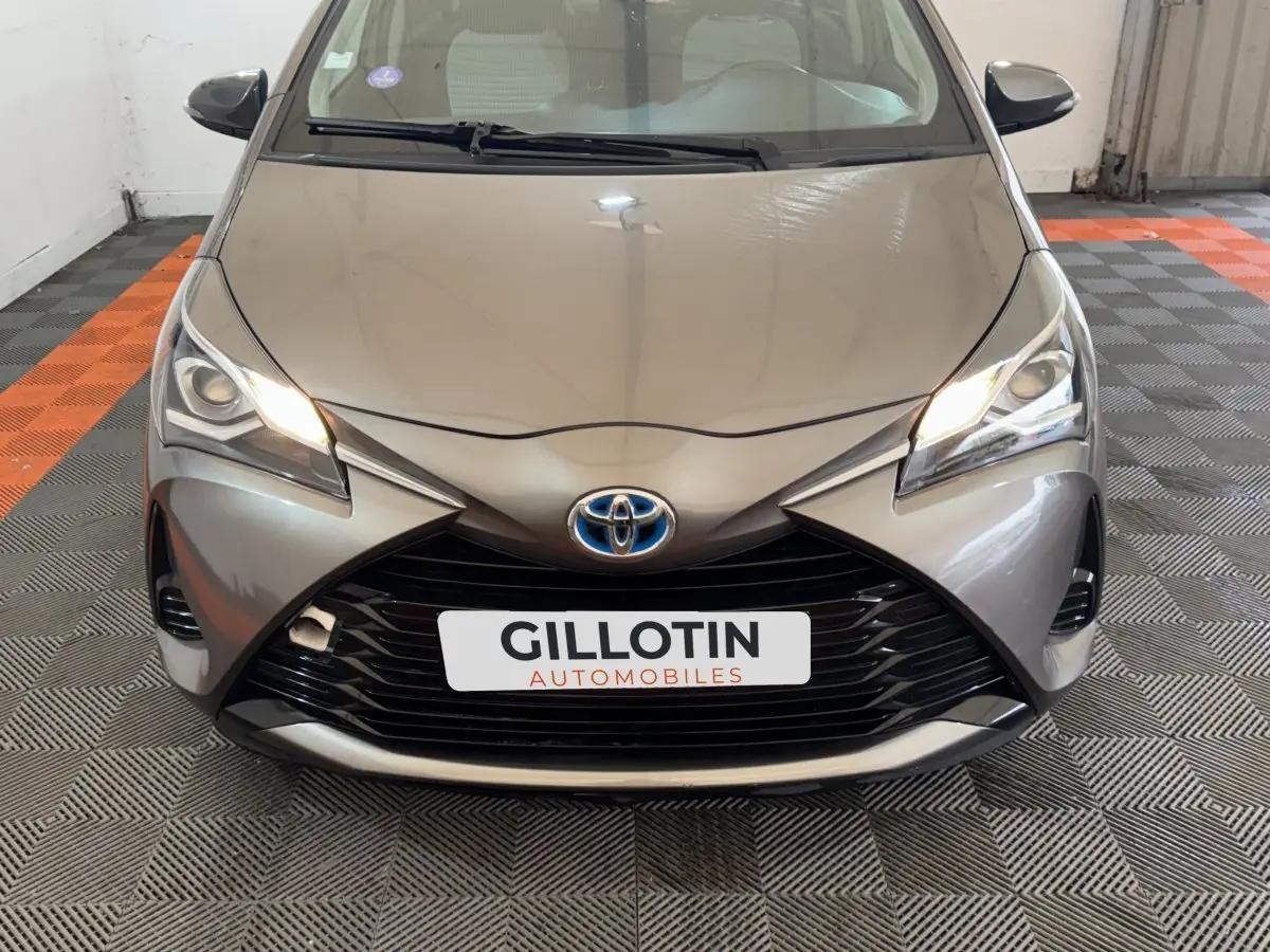 Vue avant rapprochée d’une Toyota Yaris hybride gris foncé avec phares allumés et calandre noire distinctive.