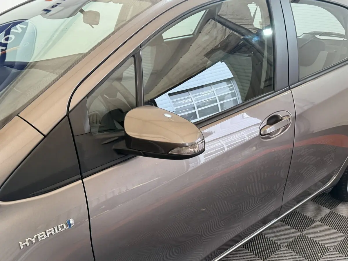 Vue latérale gauche rapprochée d’une Toyota Yaris hybride gris foncé avec rétroviseur et badge Hybrid visibles.