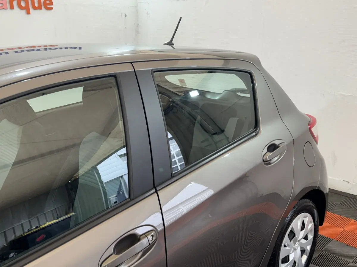 Vue latérale droite sur l'arrière d'une Toyota Yaris gris foncé avec poignée de porte et jante visible.