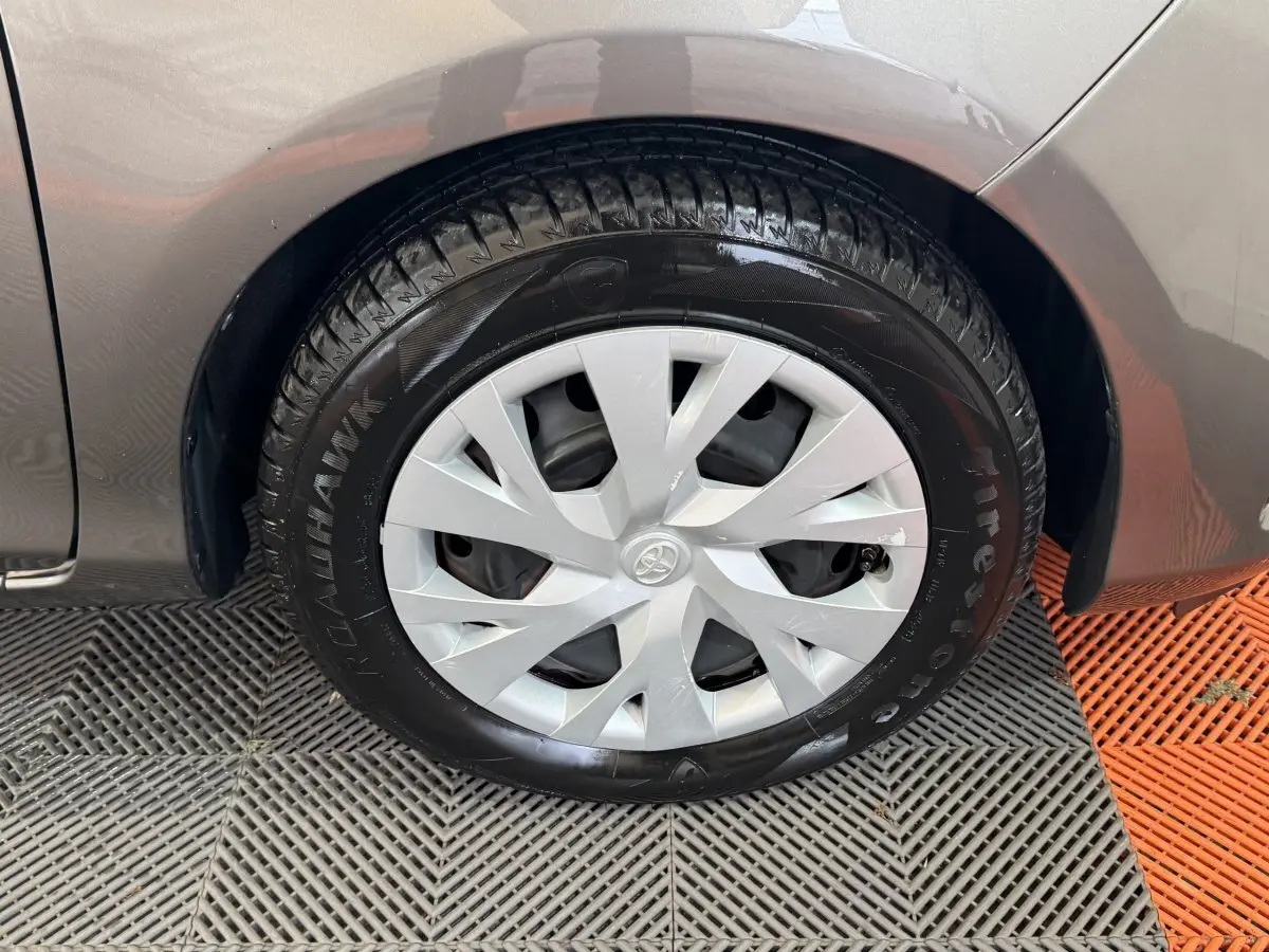 Gros plan sur la roue avant droite d’une Toyota Yaris gris foncé, mettant en valeur la jante en plastique et le pneu Firestone.
