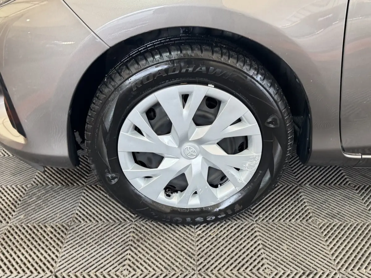 Gros plan sur la roue avant droite d'une Toyota Yaris gris foncé, avec enjoliveur argenté et pneu Firestone.