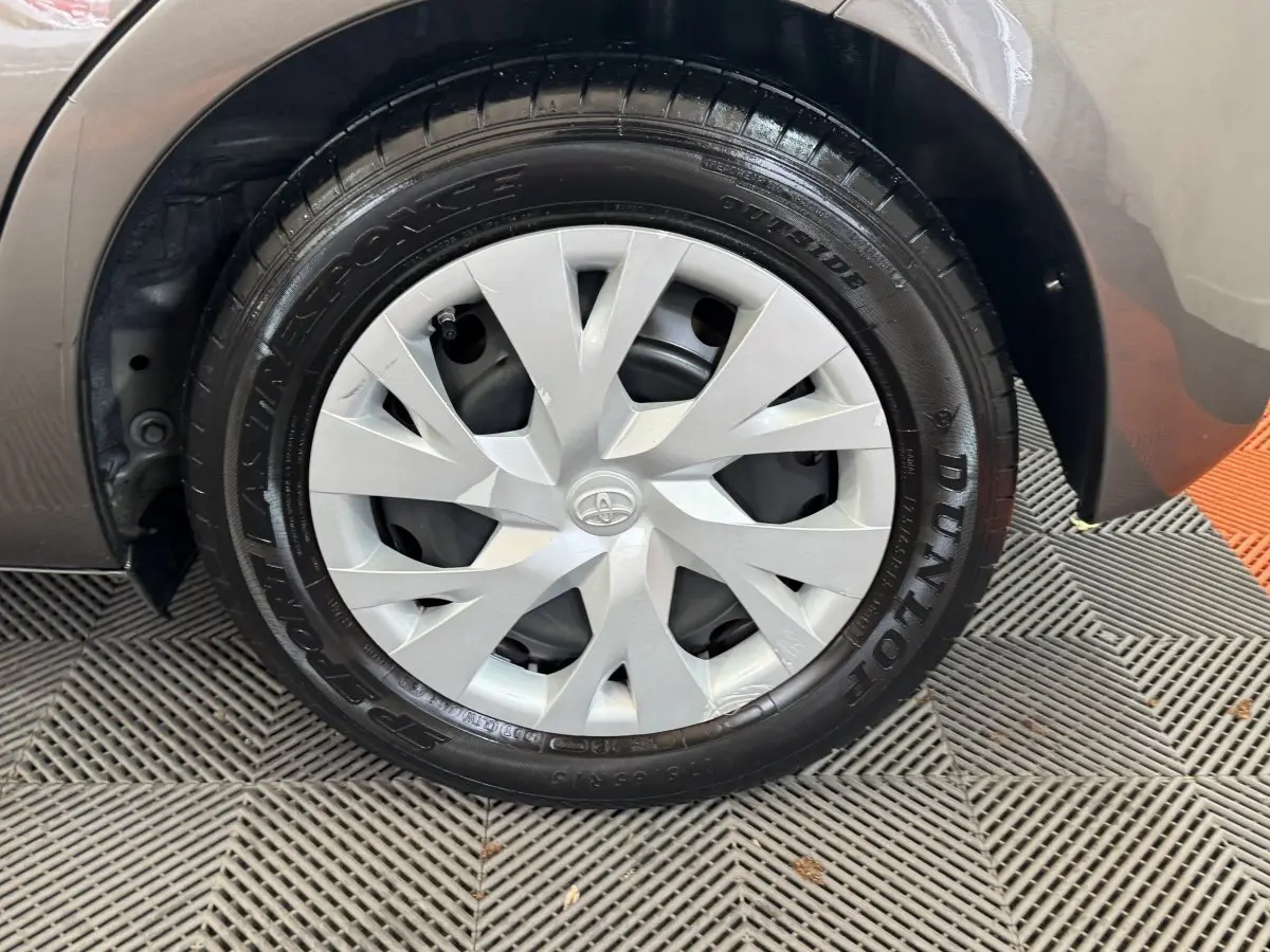 Gros plan sur la roue avant droite d'une Toyota Yaris gris foncé, avec enjoliveur argenté et pneu Dunlop.