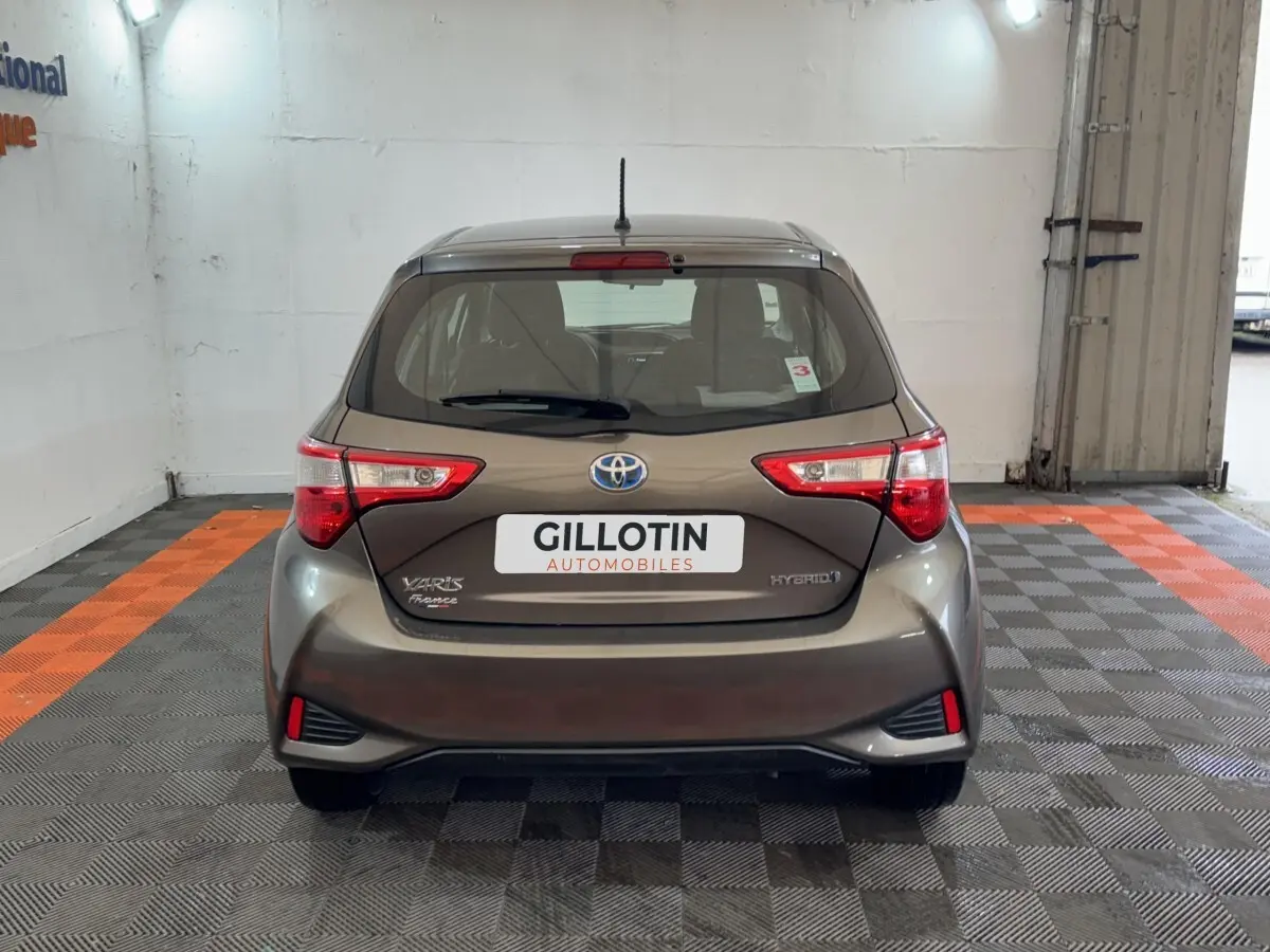 Vue arrière d'une Toyota Yaris 1.5 VVT-I Hybrid gris foncé, avec feux arrière distinctifs et logo Toyota visible.
