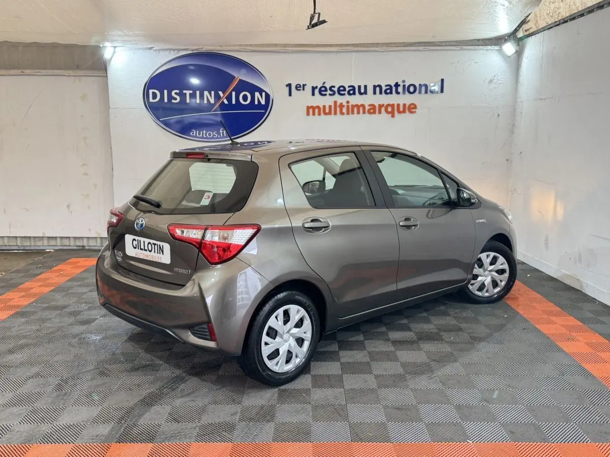Toyota Yaris 1.5 VVT-I Hybrid gris foncé vue 3/4 arrière droit dans un showroom intérieur.