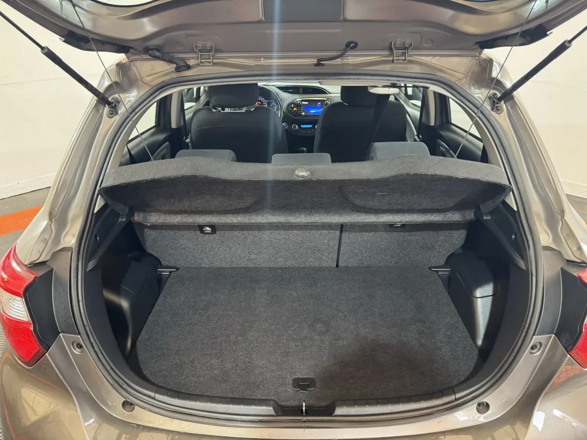 Vue arrière ouverte de la Toyota Yaris 1.5 VVT-I Hybrid gris foncé, montrant le coffre et l'intérieur avec tableau de bord éclairé.