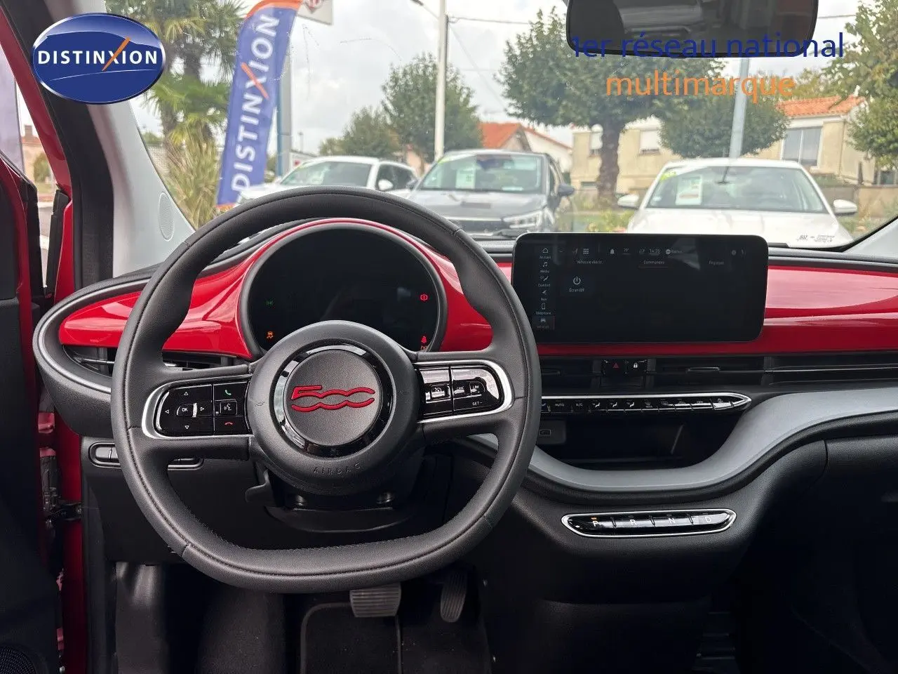 Intérieur de la FIAT 500e 2024 vue de face, tableau de bord rouge vif avec volant multifonction et écran tactile large.