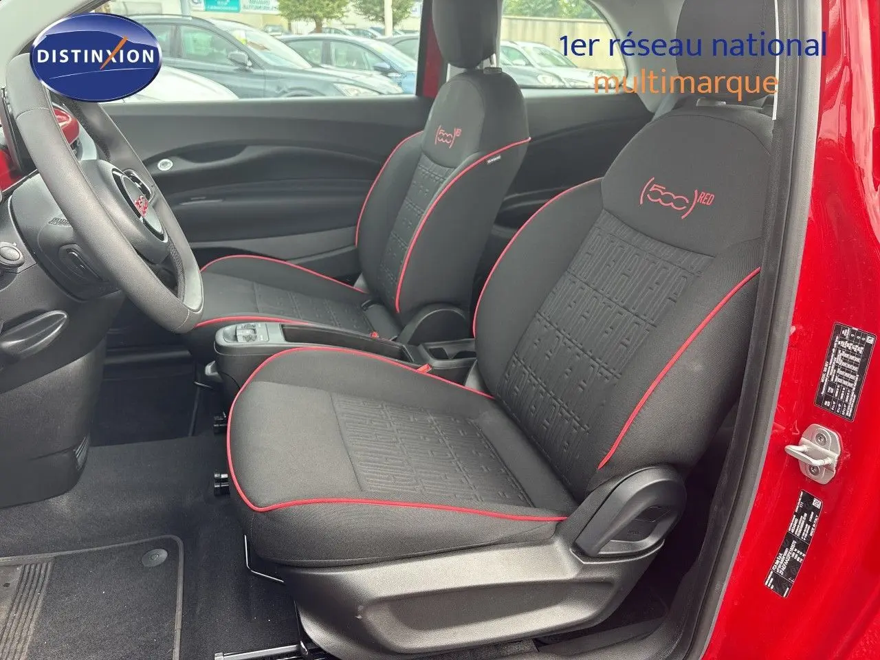 Vue intérieure côté conducteur de la FIAT 500e rouge 2024, sièges noirs avec surpiqûres rouges et logo 500 (RED) brodé.