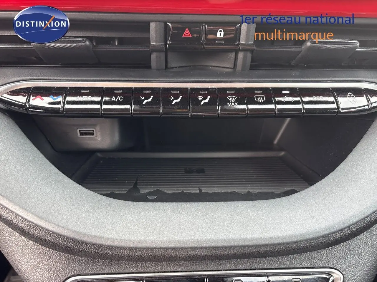 Vue rapprochée de la console centrale de la FIAT 500e rouge 2024, avec commandes climatisation et rangements visibles.