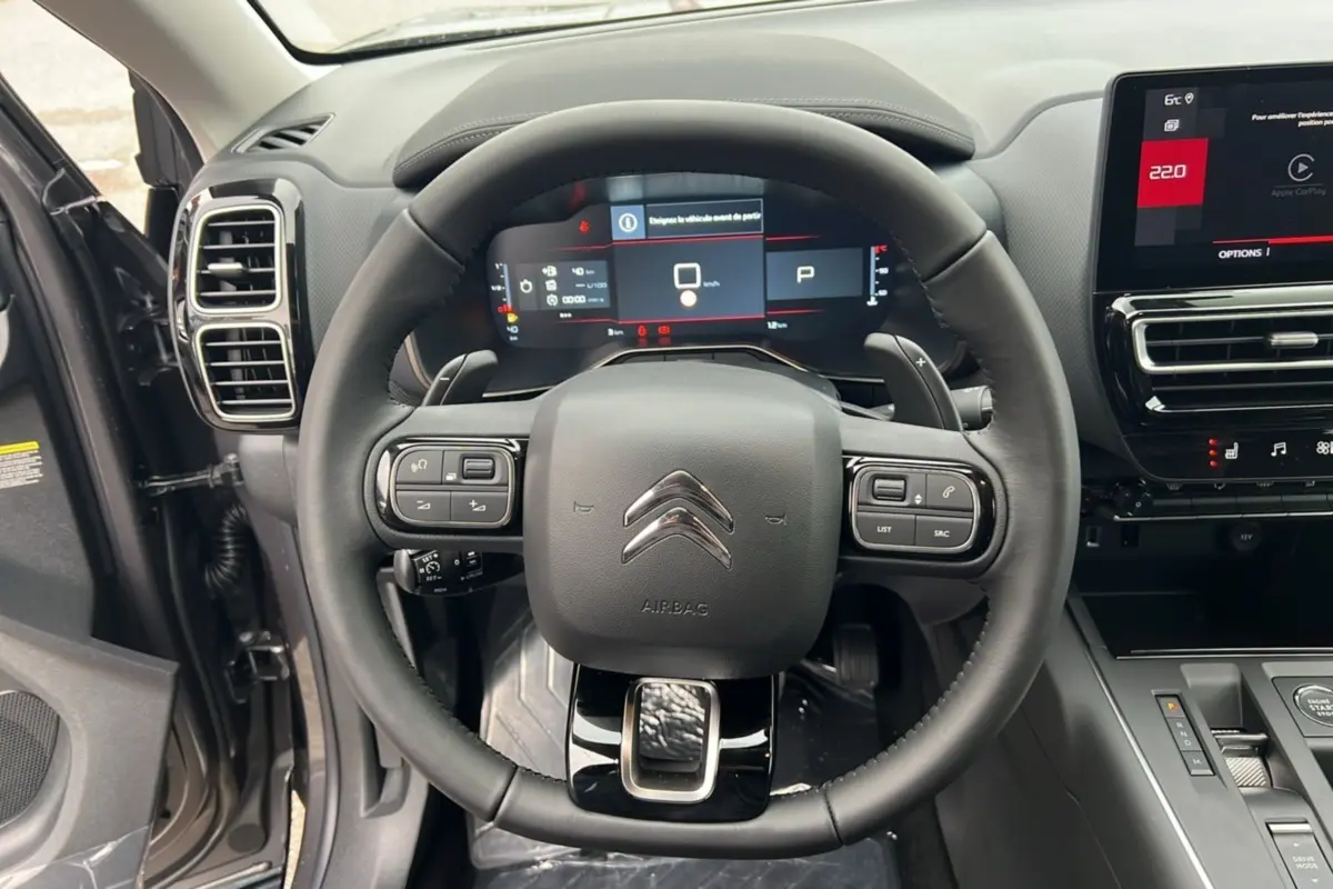 Vue intérieure centrée sur le volant du Citroën C5 Aircross Hybrid 2025, avec tableau de bord numérique et commandes intégrées.