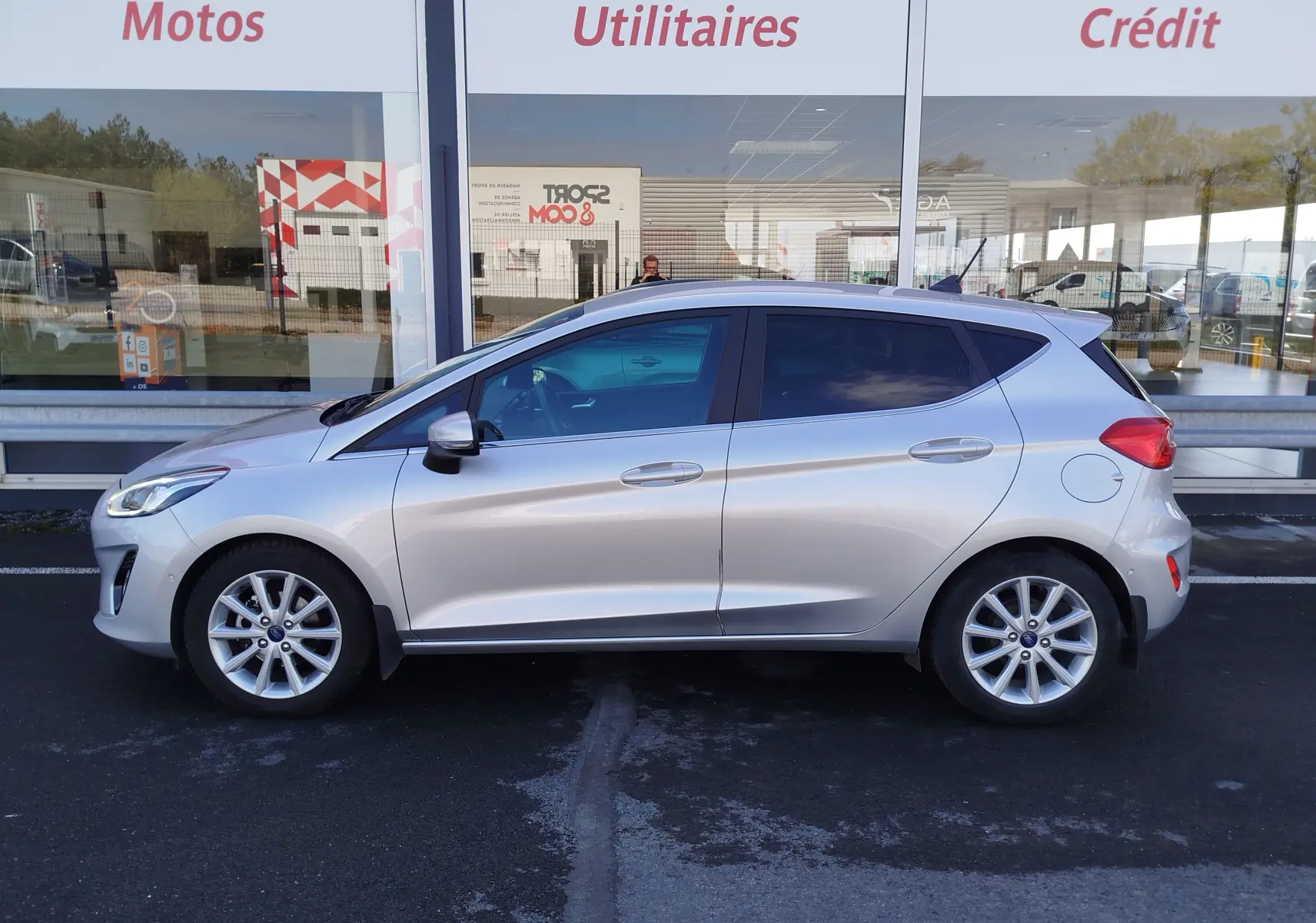 Profil côté gauche d'une Ford Fiesta gris lunaire 2019, finition Titanium, garée devant une vitrine commerciale.