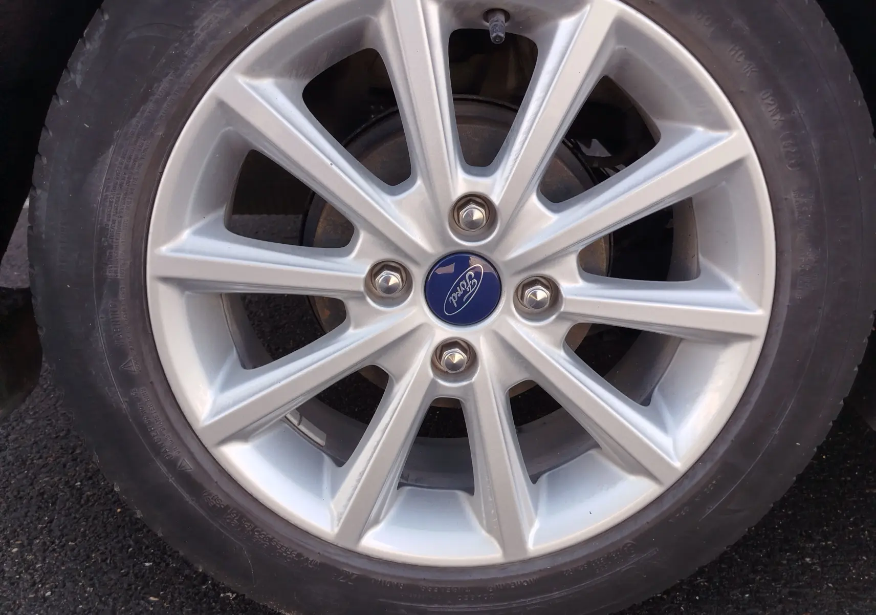 Gros plan sur la jante alliage argentée d'une Ford Fiesta gris lunaire avec logo Ford bleu au centre.