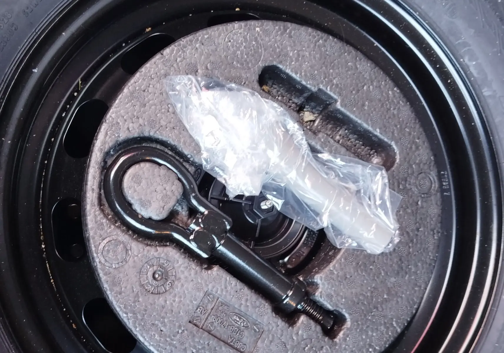 Gros plan sur la roue de secours noire d’une Ford Fiesta gris lunaire avec outil de remorquage fixé au centre.