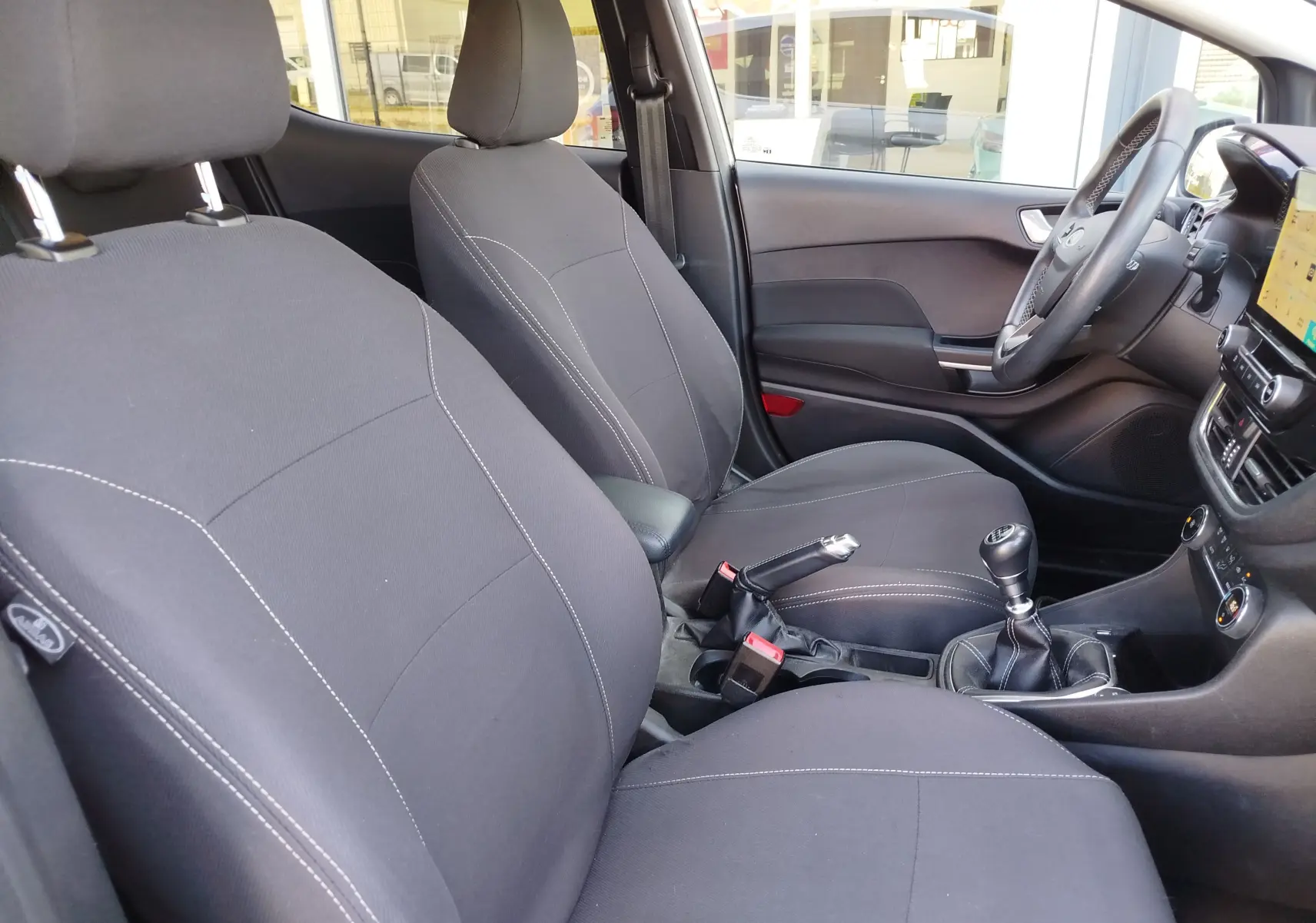 Vue intérieure côté gauche de la Ford Fiesta 2019, sièges tissu gris foncé avec coutures blanches et boîte manuelle.