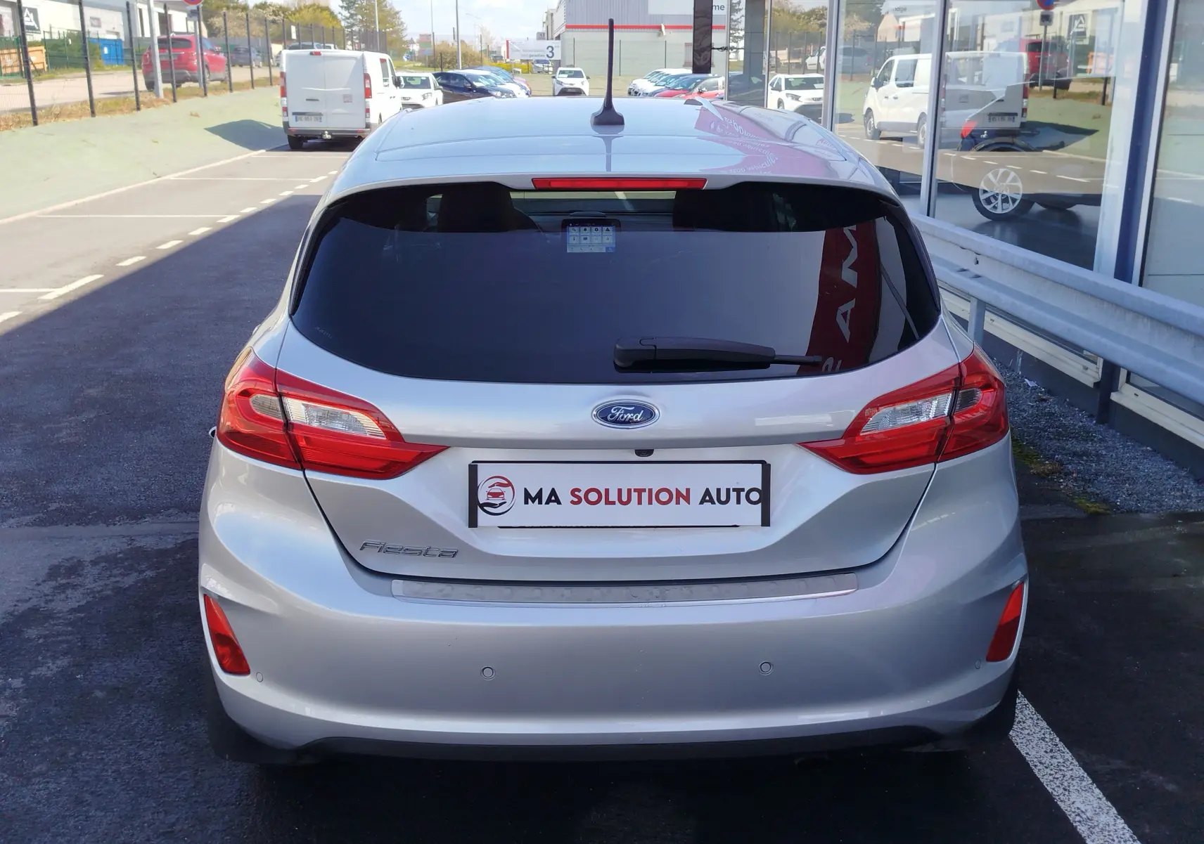 Vue arrière d'une Ford Fiesta gris lunaire 2019 avec feux arrière allongés et vitre arrière teintée, stationnée en extérieur.