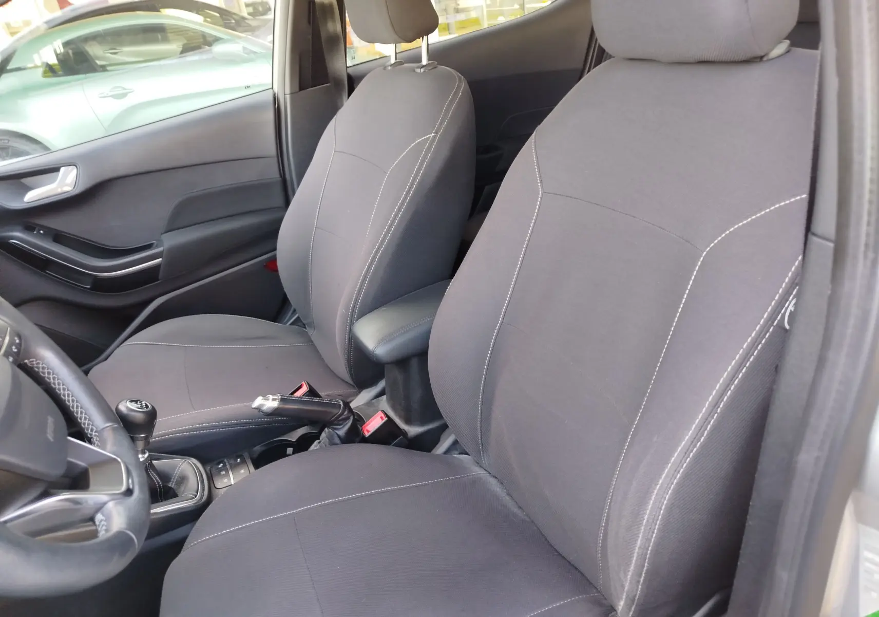 Vue intérieure de la Ford Fiesta 2019, montrant les sièges avant noirs avec surpiqûres blanches et levier de vitesse manuel.