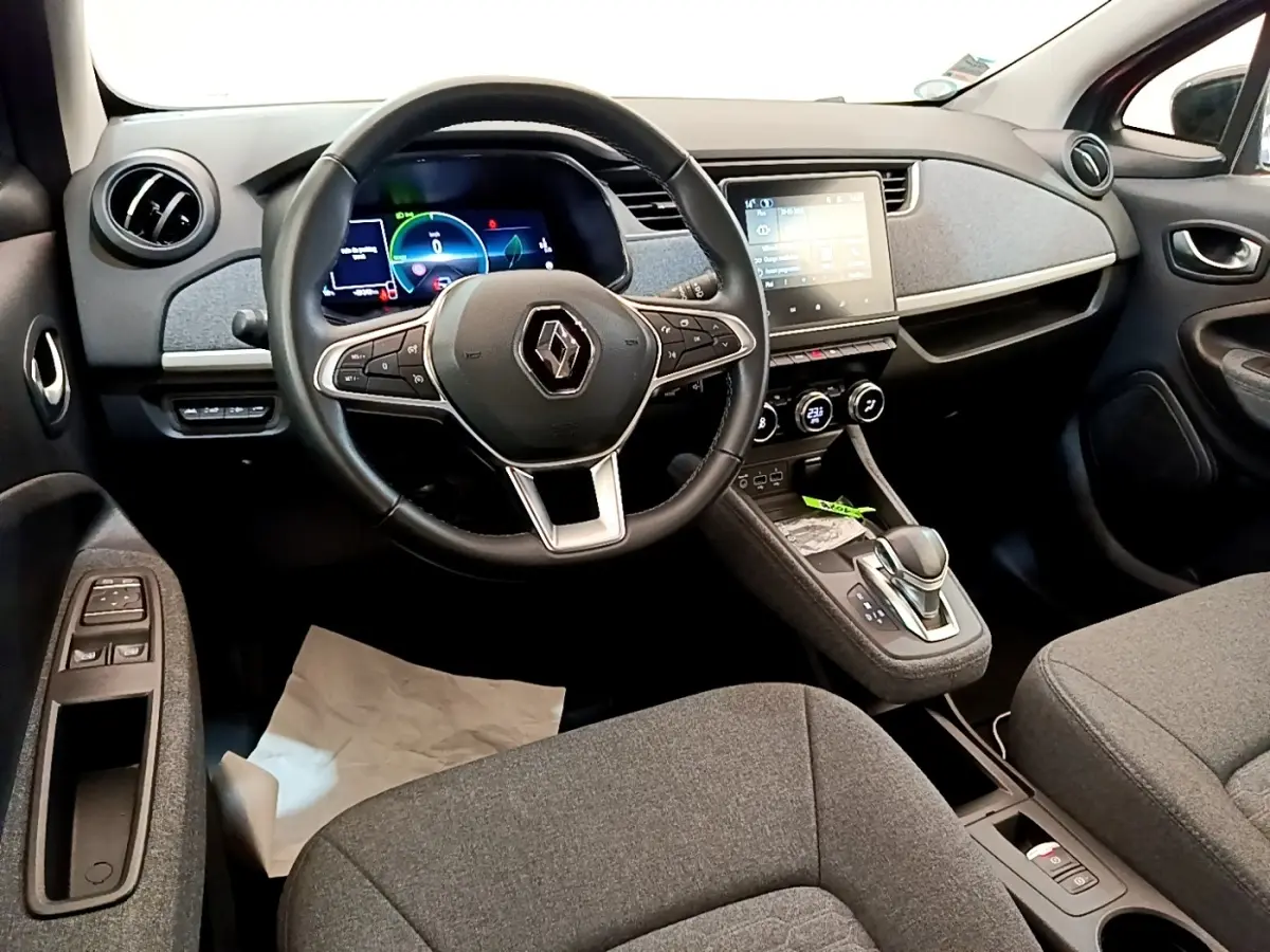 Vue intérieure avant de la Renault ZOE gris clair, montrant le volant, tableau de bord digital et écran tactile central.