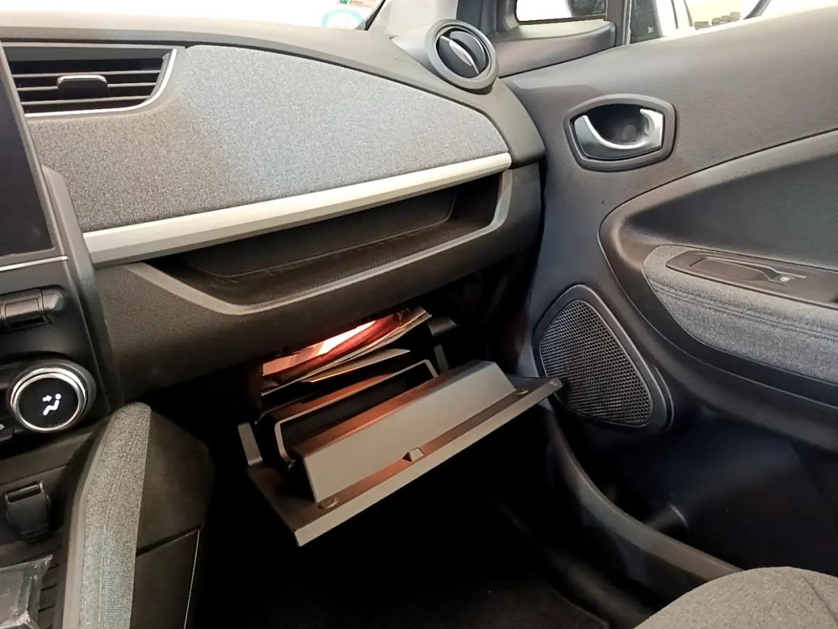 Intérieur de la Renault ZOE gris clair, vue côté passager avec boîte à gants ouverte et tableau de bord texturé.