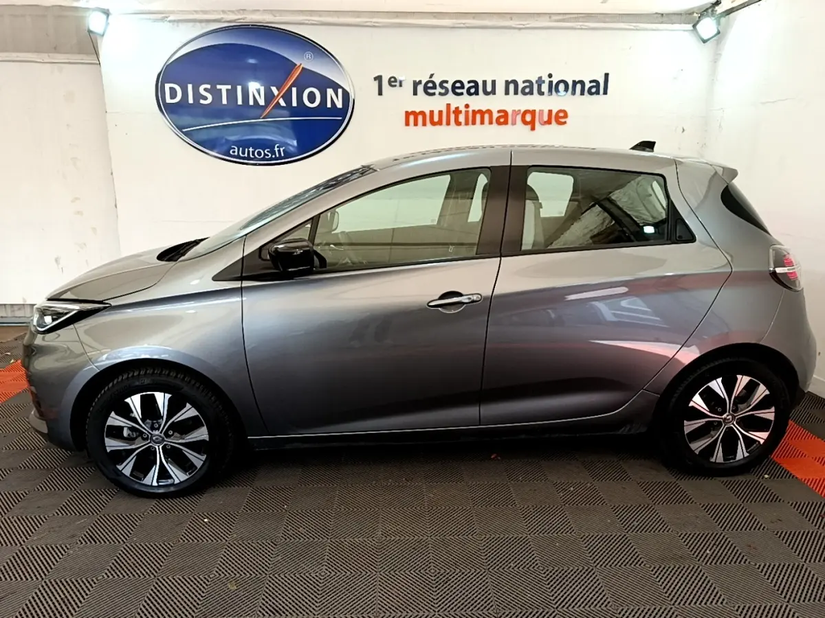 Vue de profil côté gauche d'une Renault ZOE gris clair Evolution R110 2022 en intérieur avec jantes noires et argentées.