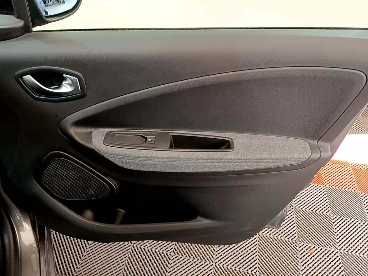 Vue rapprochée de la porte intérieure côté conducteur de la Renault ZOE gris clair, avec panneau tissu gris et commande de fenêtre.