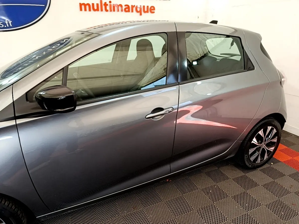 Profil côté gauche d'une Renault ZOE gris clair 2022, avec rétroviseur noir et jantes alliage visibles.