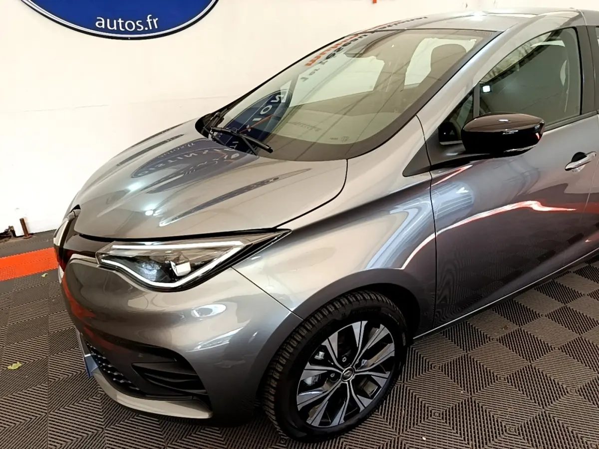 Vue 3/4 avant droit d'une Renault ZOE gris clair avec jantes noires et phares LED distinctifs.