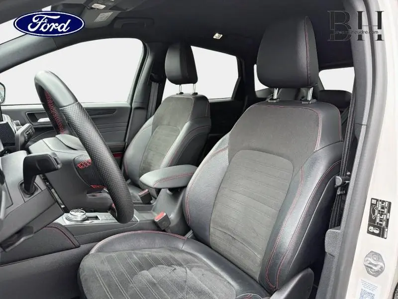 Vue intérieure côté gauche du Ford Kuga blanc, sièges sport noir avec surpiqûres rouges et volant cuir perforé.