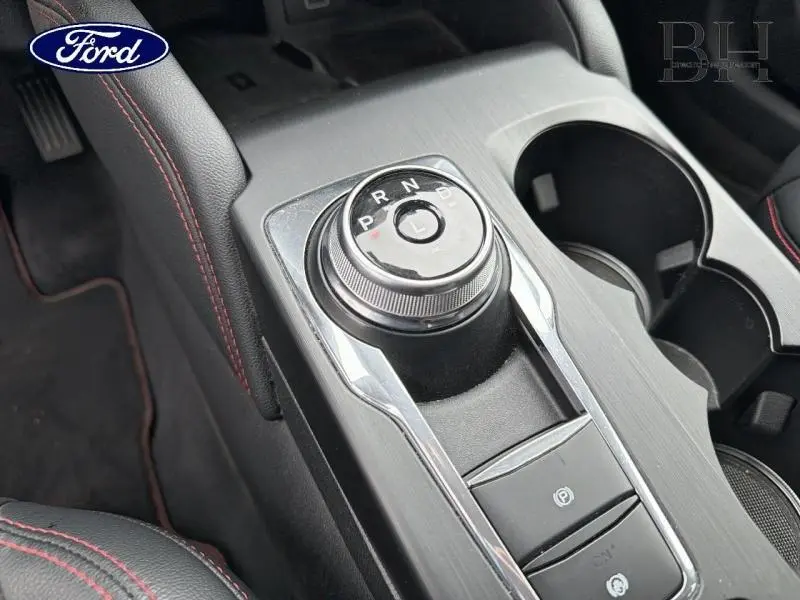 Vue rapprochée de la console centrale du Ford Kuga blanc, mettant en valeur la molette de boîte automatique et les surpiqûres rouges.