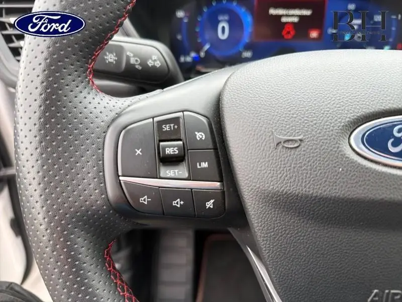 Gros plan sur le volant cuir noir perforé avec surpiqûres rouges du Ford Kuga 2023, mettant en valeur les commandes multifonctions.