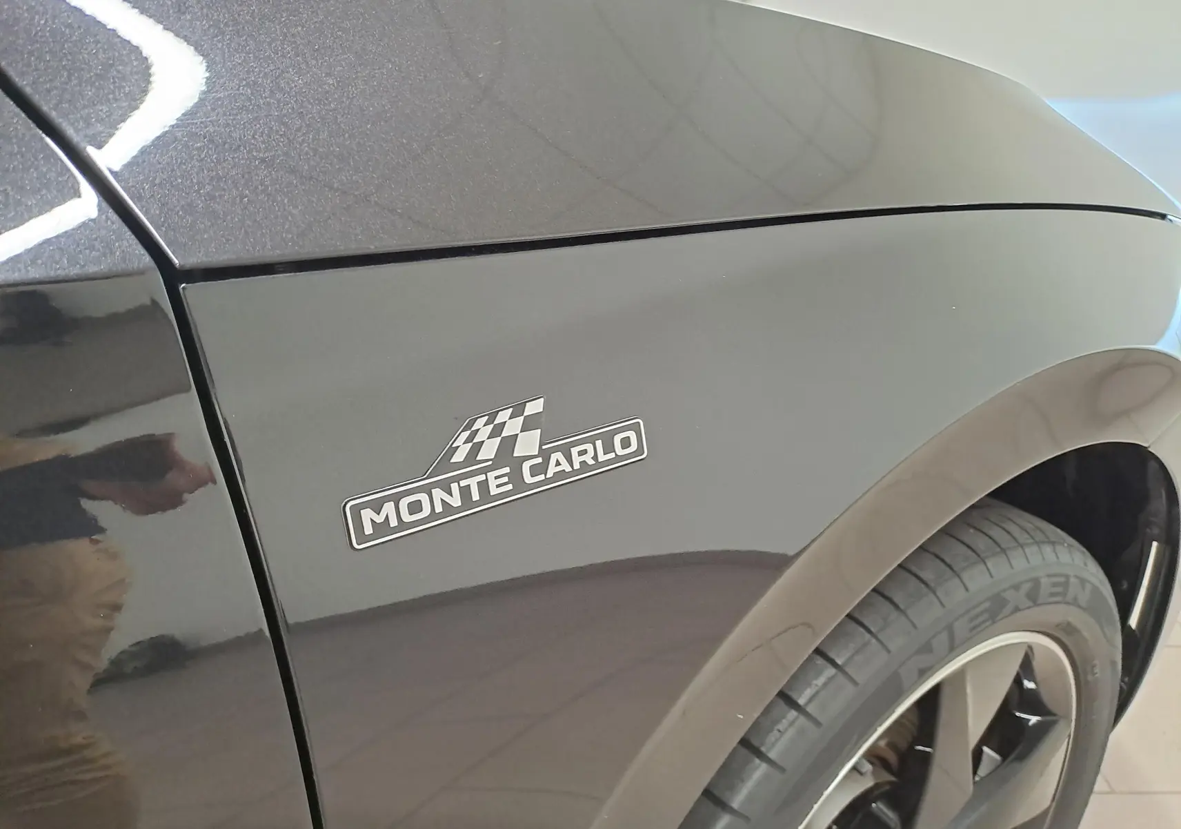 Gros plan sur l'aile avant gauche noire nacrée d'une Skoda Scala Monte-Carlo avec logo distinctif et jante noire.