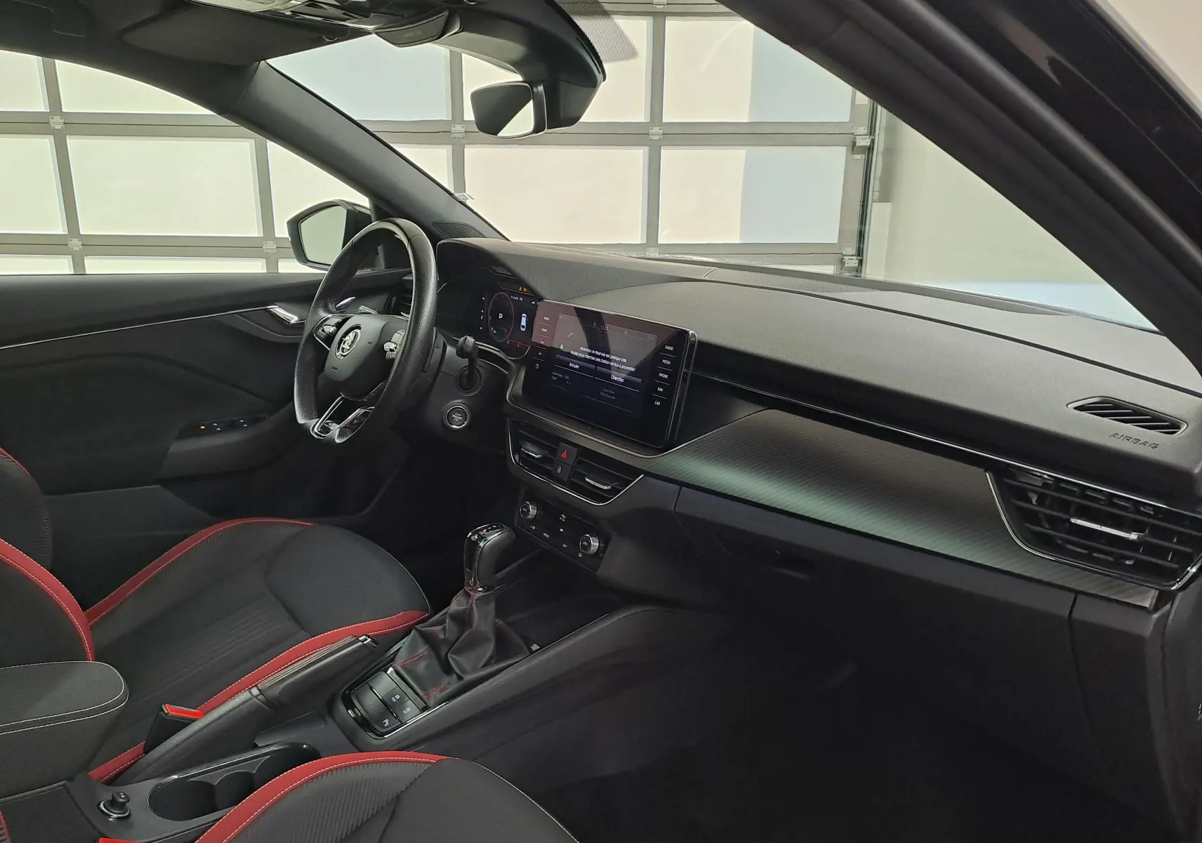 Intérieur de la Skoda Scala 2022 vu côté conducteur, sièges noirs avec surpiqûres rouges et tableau de bord moderne.