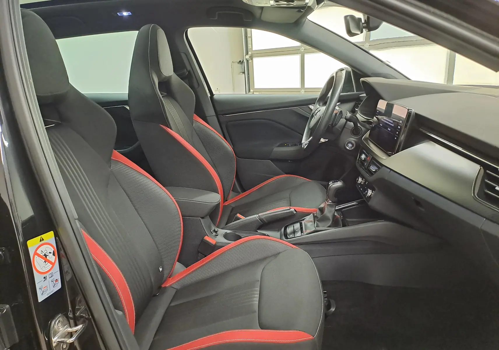 Vue intérieure côté gauche de la Skoda Scala 2022 avec sièges sport noirs et surpiqûres rouges, tableau de bord moderne.