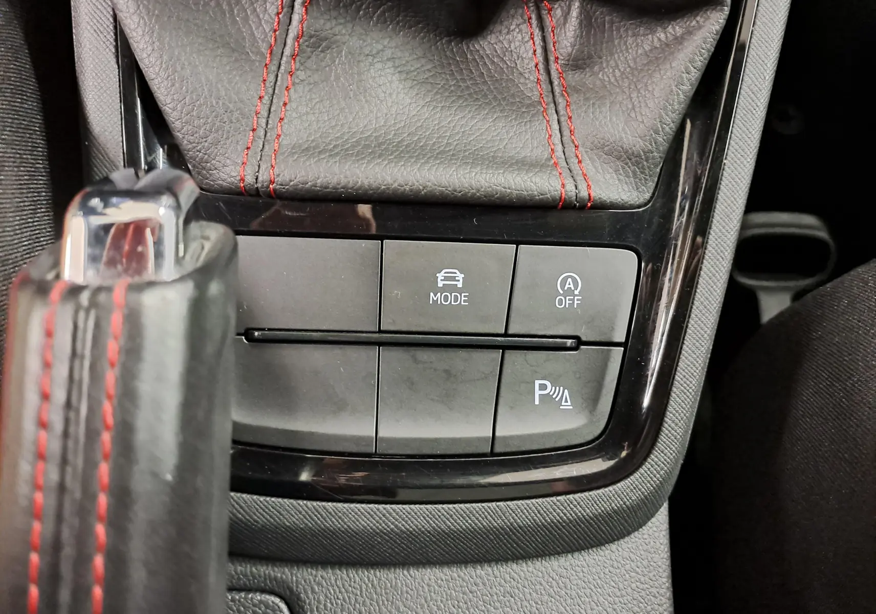 Gros plan sur la console centrale de la Skoda Scala 2022 avec coutures rouges et boutons de mode de conduite et parking assist.