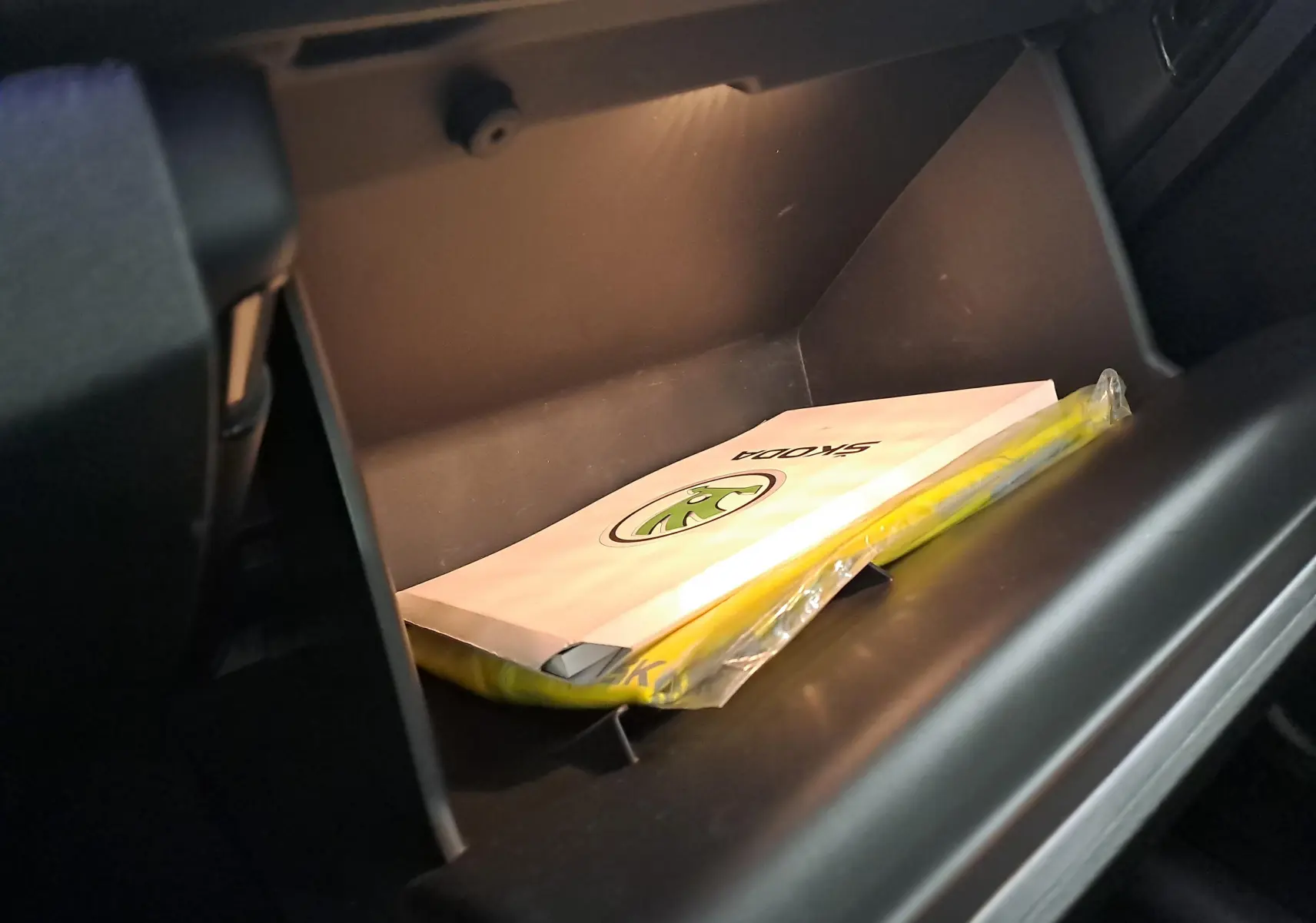 Vue rapprochée de la boîte à gants ouverte d'une Skoda Scala noire avec manuel et gilet jaune à l'intérieur.